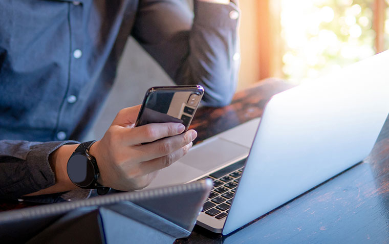 Man sitting in front of a laptop, a tablet, and holding a mobile phone